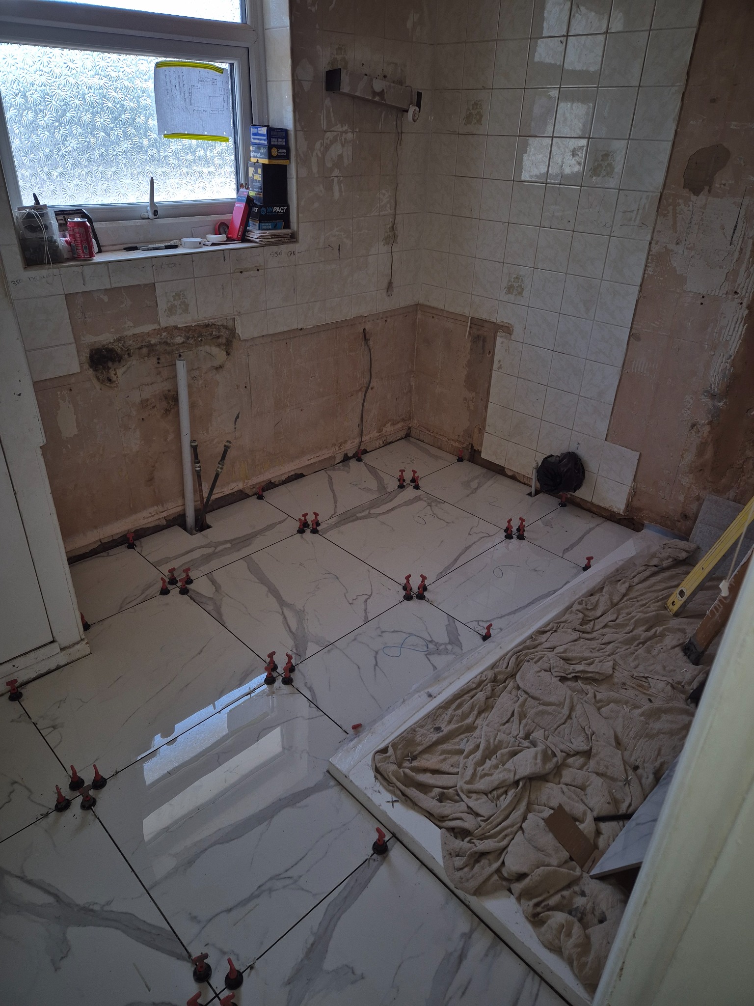Large-format floor tiles laid over the prepared floor as the waterproofed bathroom build progresses
