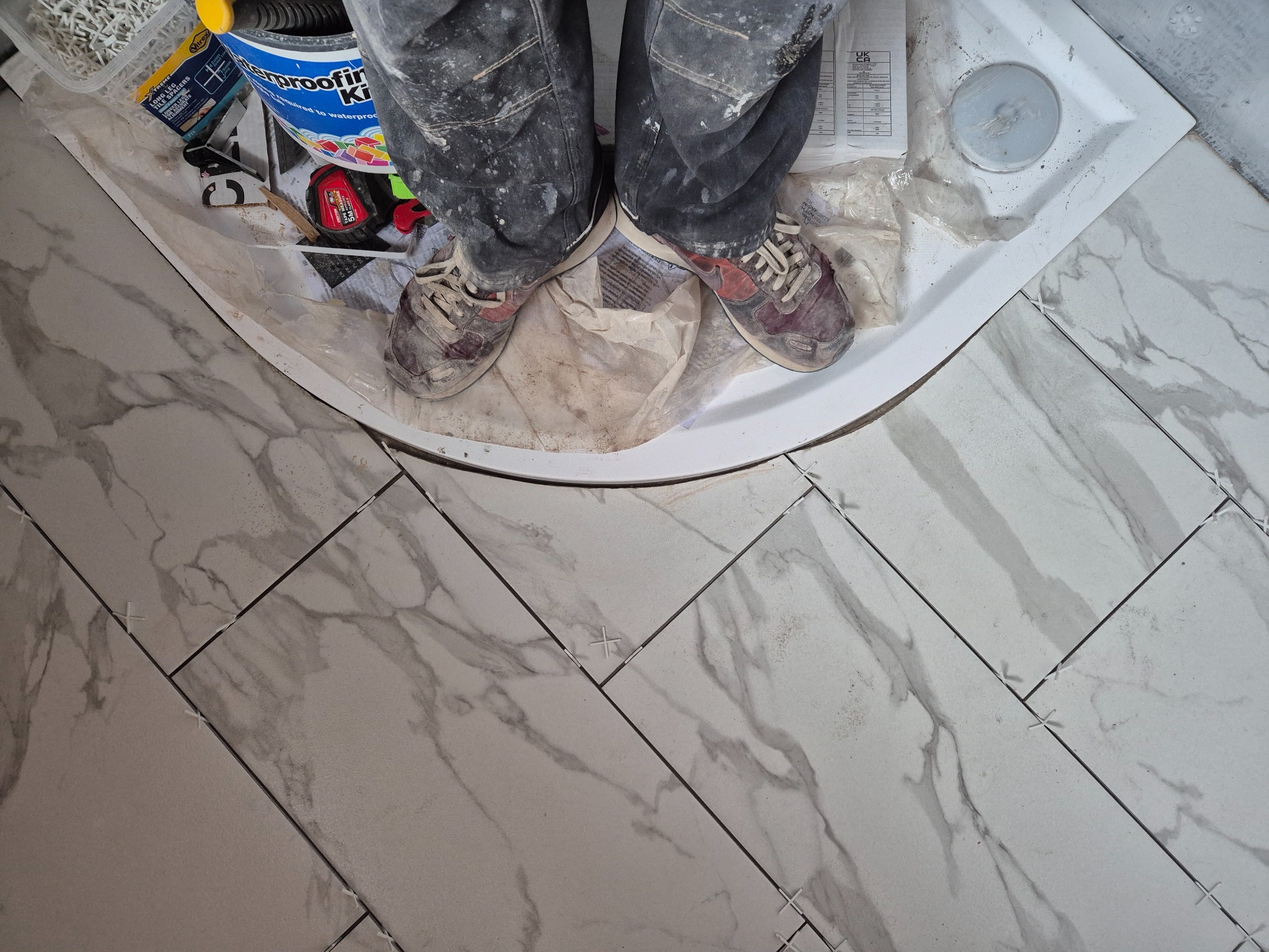 Prepared shower-tray perimeter carried into the floor tiling stage with neat cuts around the curved edge